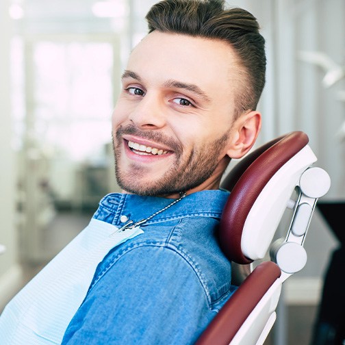 Man with denim jacket sitting in dental chair and smiling