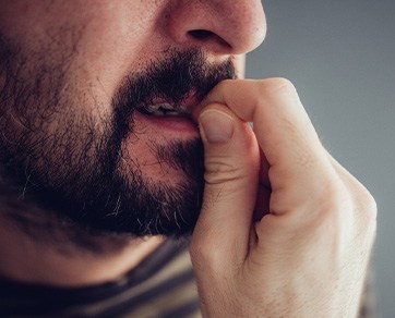 Man with facial hair chewing his fingernails