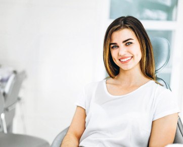 Woman in white shirt sitting in dental chair and smiling