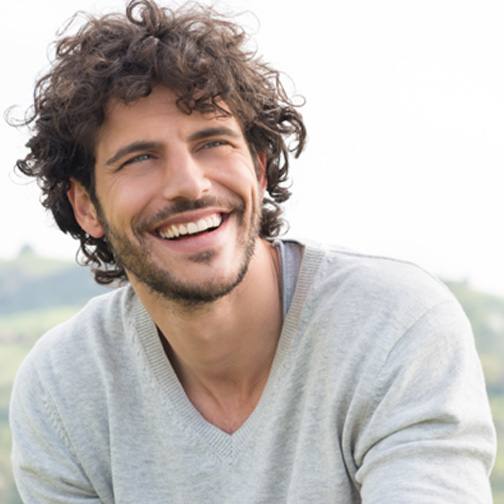 Young man with beard sitting outside and smiling