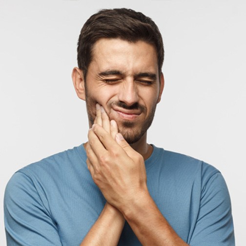 Man in blue shirt rubbing jaw in pain