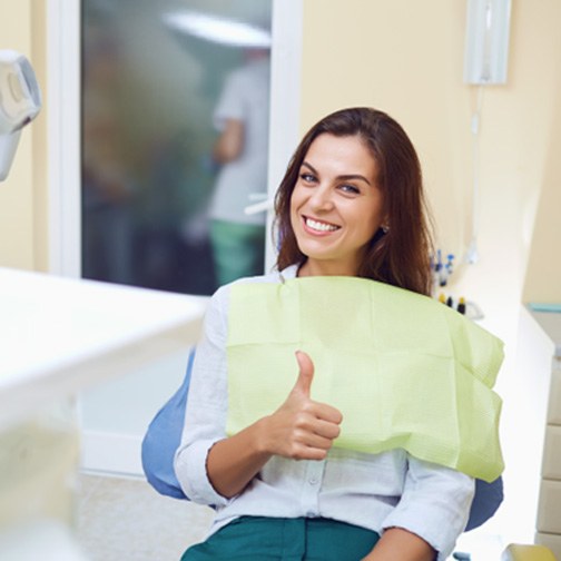 Female dental patient in treatment chair giving thumbs up