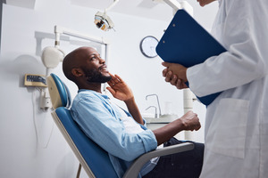 Dental patient looking up at dentist while rubbing jaw